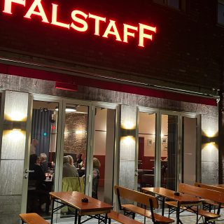 Außenansicht des Falstaff mit roter Leuchtreklame, beleuchtetem Eingangsbereich und Außentischen am Abend