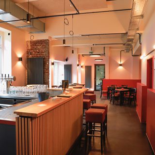 Stilvolle Bar mit Holztheke, Zapfanlage, roten Hockern und warm beleuchtetem Gastraum mit Backsteinakzenten