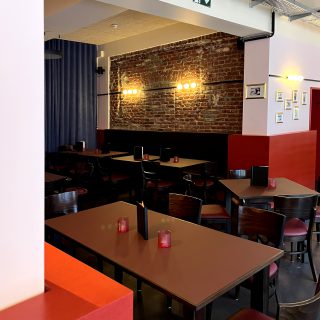 Stilvoller Gastraum mit Holztischen, roten Stühlen, dekorativen Kerzen und beleuchteter Backsteinwand im Hintergrund