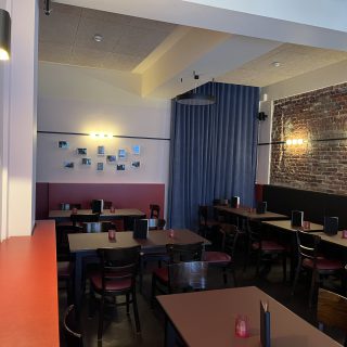 Modern eingerichteter Gastraum mit dunklen Holztischen, roter Wandgestaltung, Vorhang und beleuchteter Backsteinwand