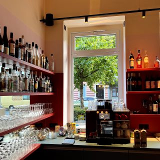 Stilvoller Barbereich mit Regalen voller Spirituosen, Kaffeemaschine und großem Fenster mit Blick auf Bäume und Straße